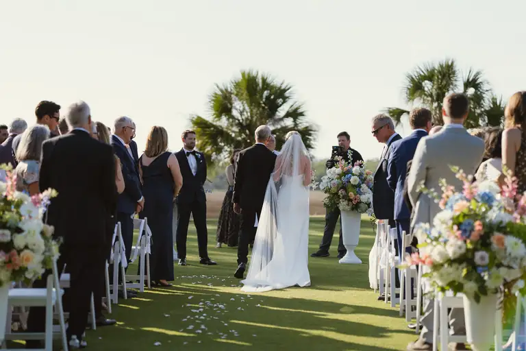 Bride walking down an outdoor aisle between guests and tall florals