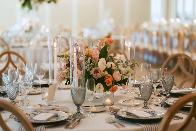 Long celebration table set with peach florals, candles and glassware