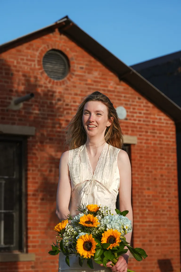 A bride holding sunflowers in front of a red brick building