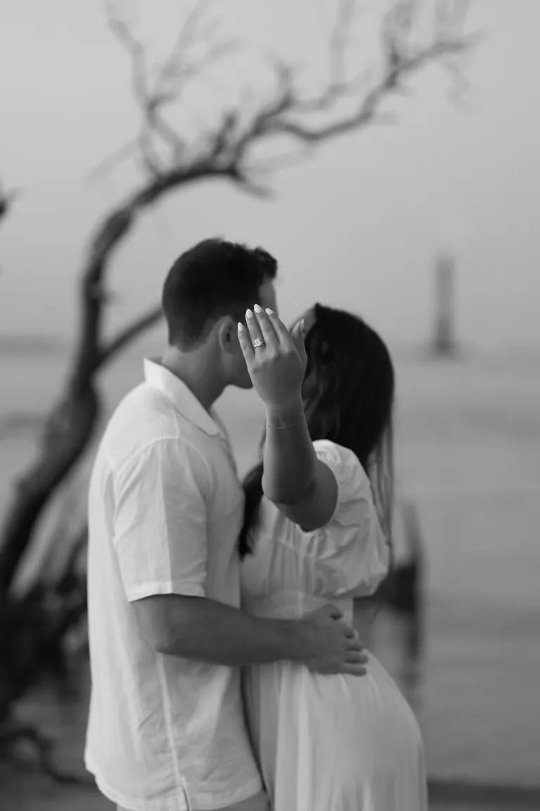 A couple embracing on the shore beneath bare branches, black and white