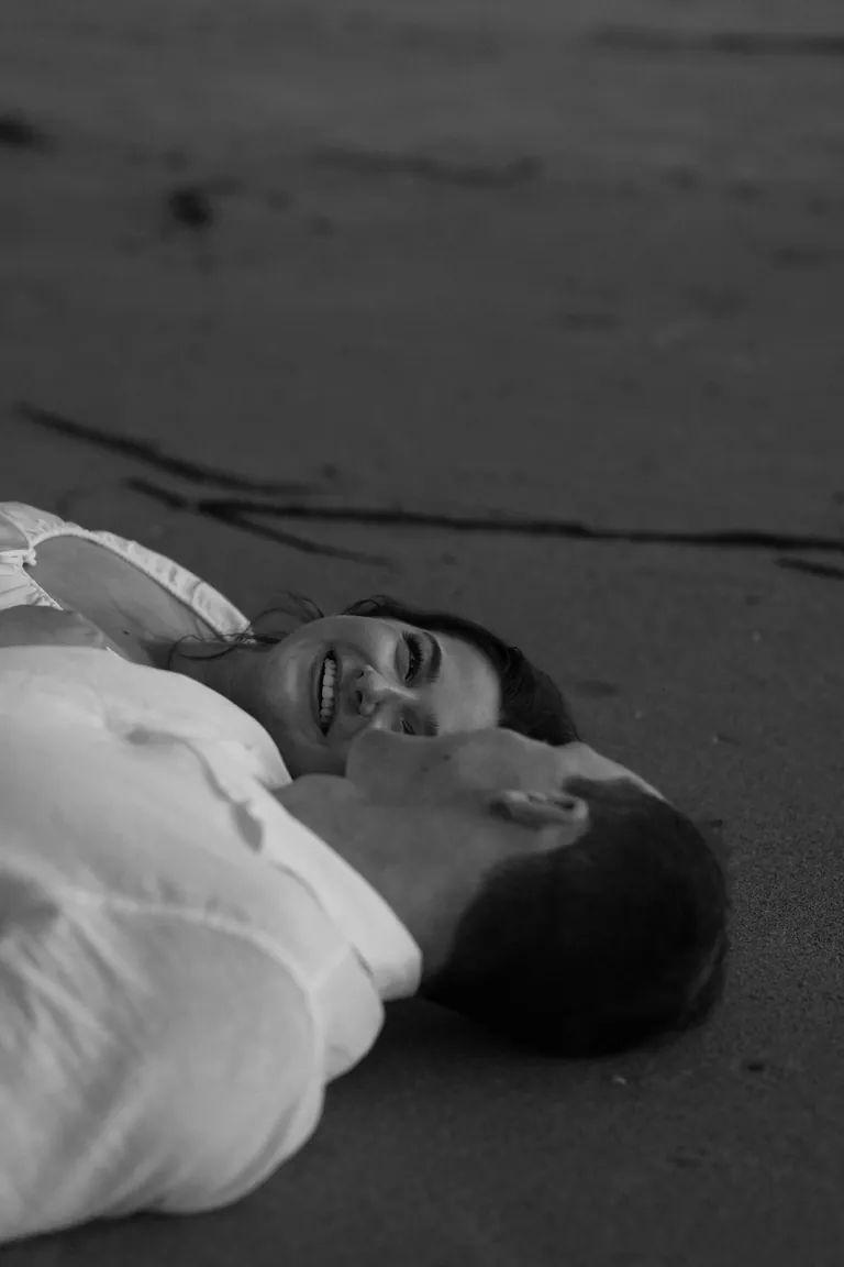 A man lying on wet sand in the evening light, black and white