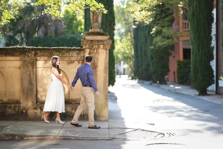 Engaged couple walking hand in hand along a historic Charleston street