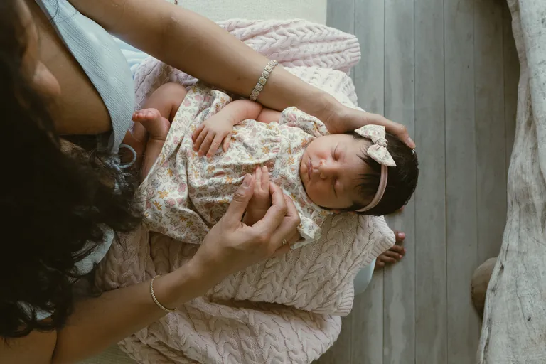 A newborn in a lace bonnet held in her mother's arms