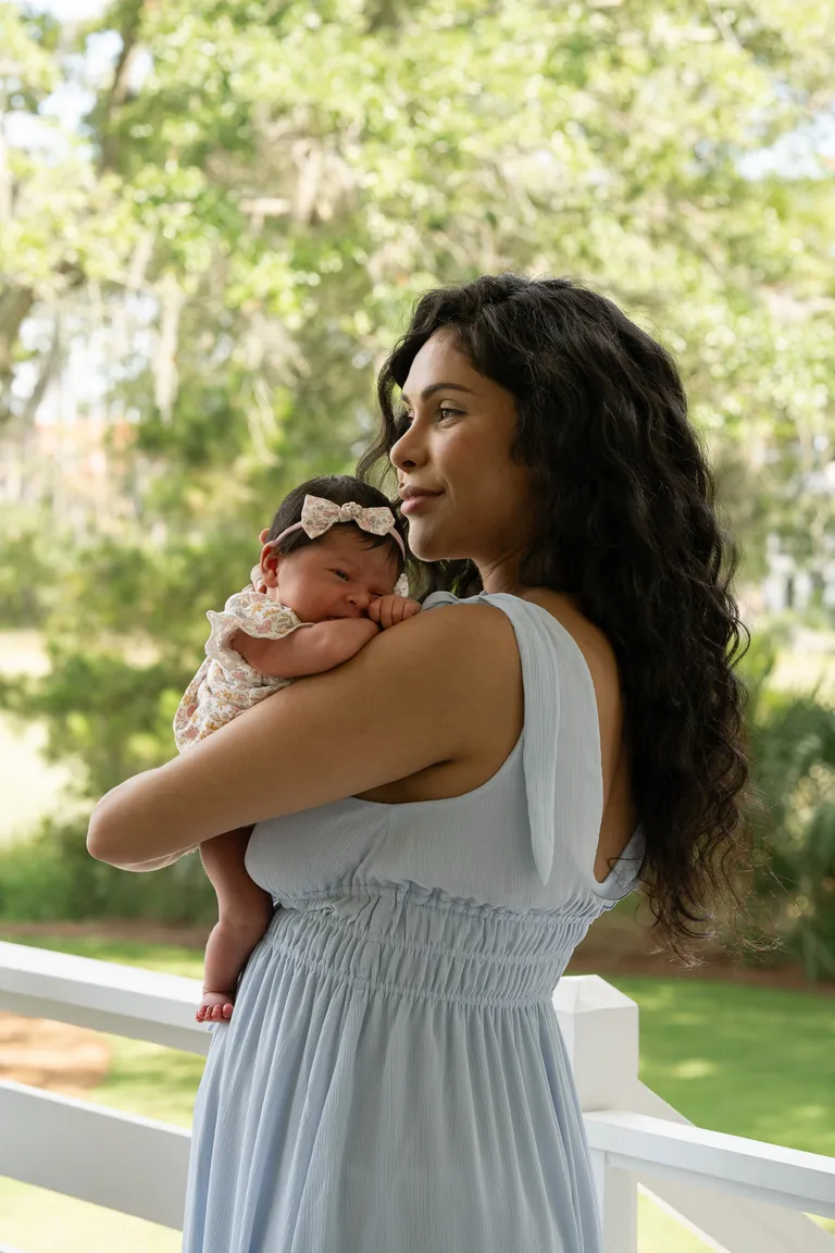 A mother in a blue dress holding her newborn on the porch