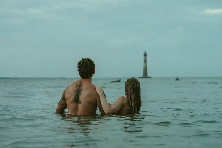 A couple in the ocean looking out toward Morris Island Lighthouse
