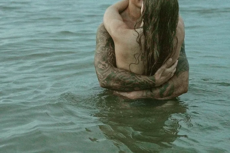 A man holding a woman close in the sea, her wet hair over her shoulder