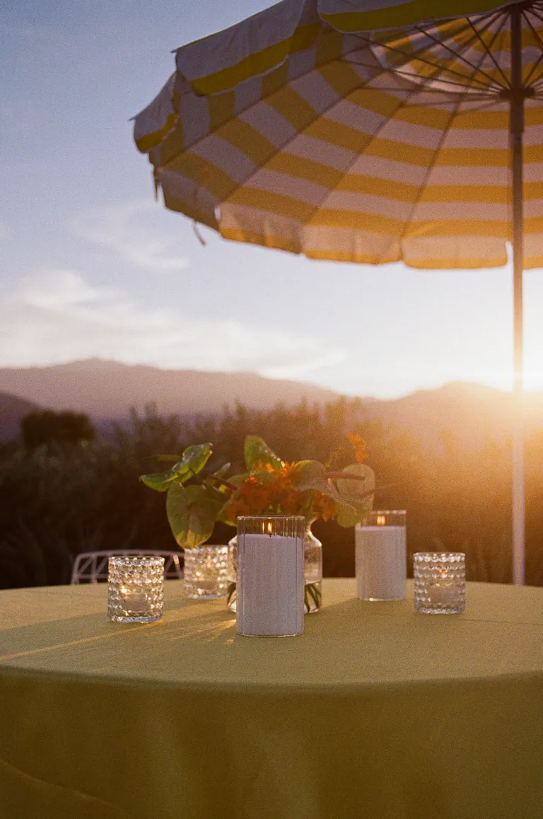 A table set under a striped umbrella as the sun sets over the mountains