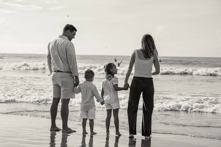 A family of four holding hands in the shallow surf, black and white