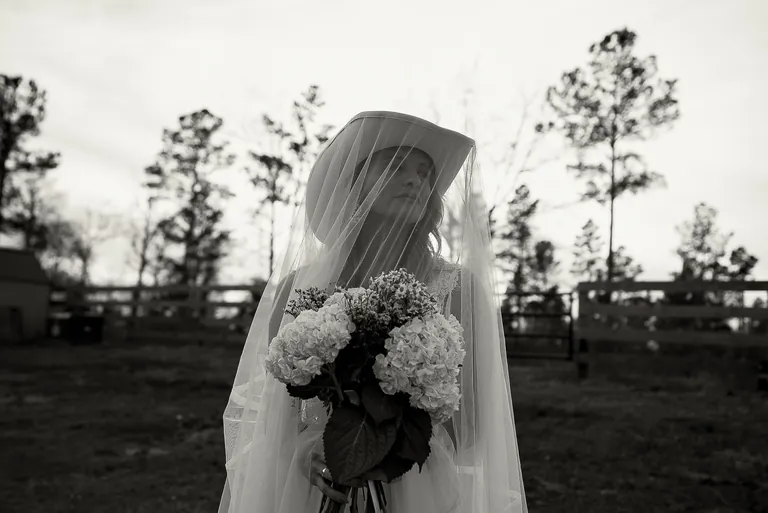 A veiled bride holding her bouquet in the marsh at dusk, black and white