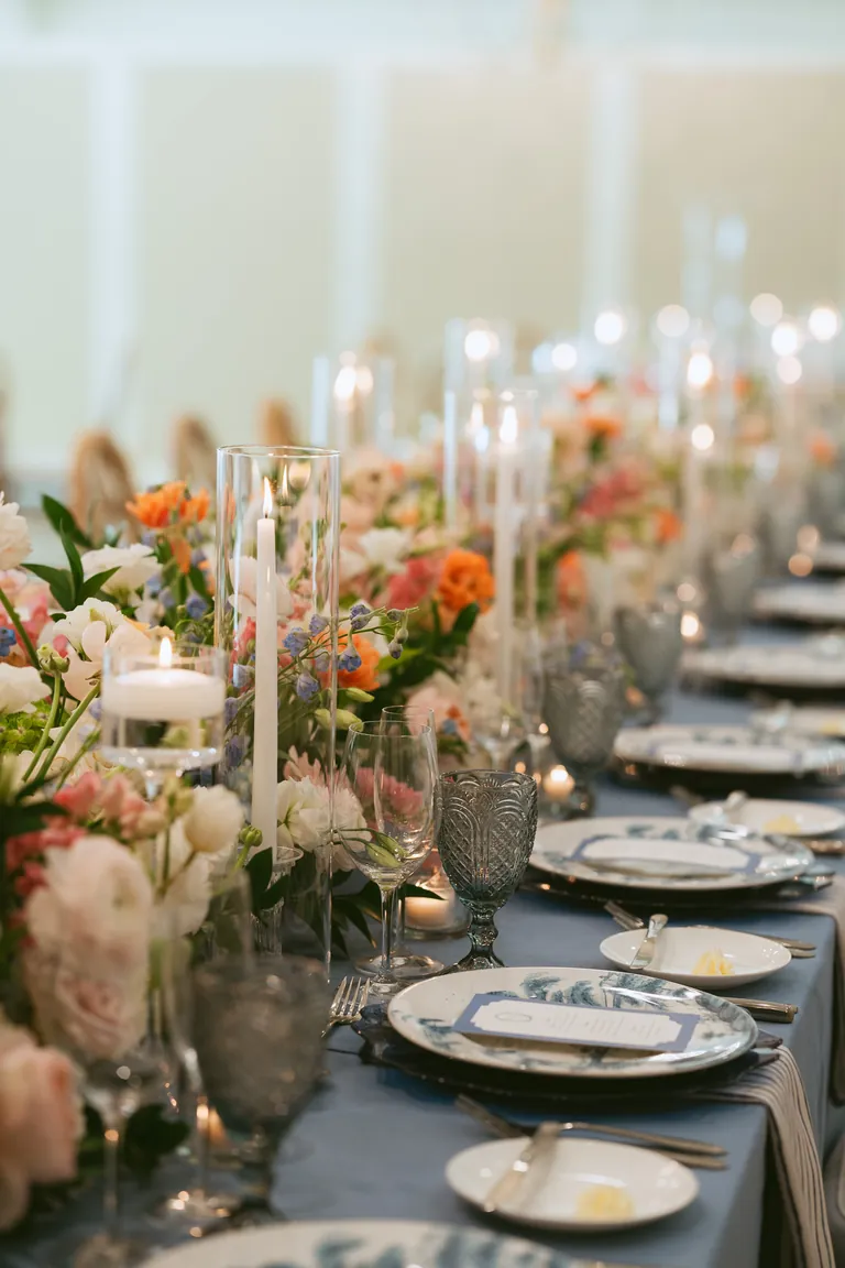 A long reception table set with candles, crystal and peach flowers