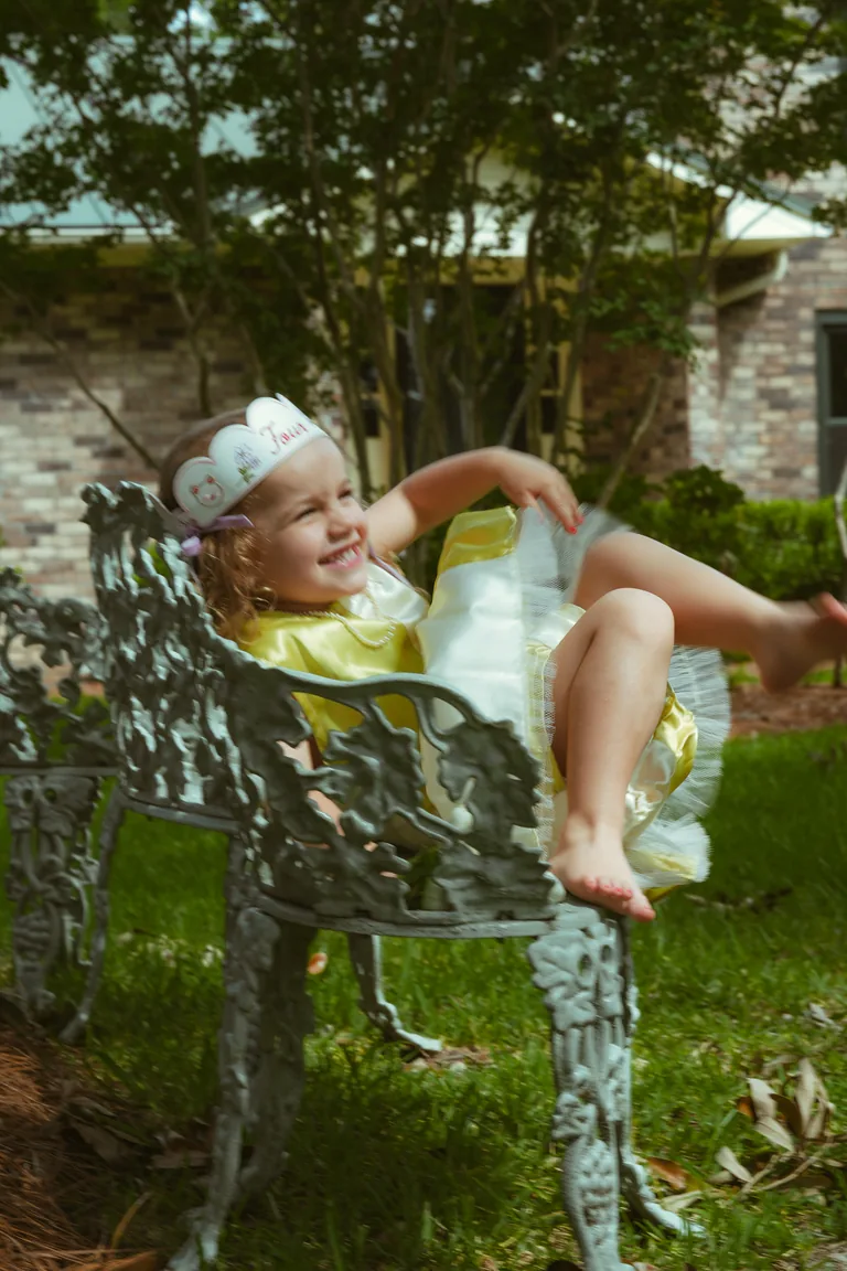 A little girl in a yellow party dress laughing on a garden bench